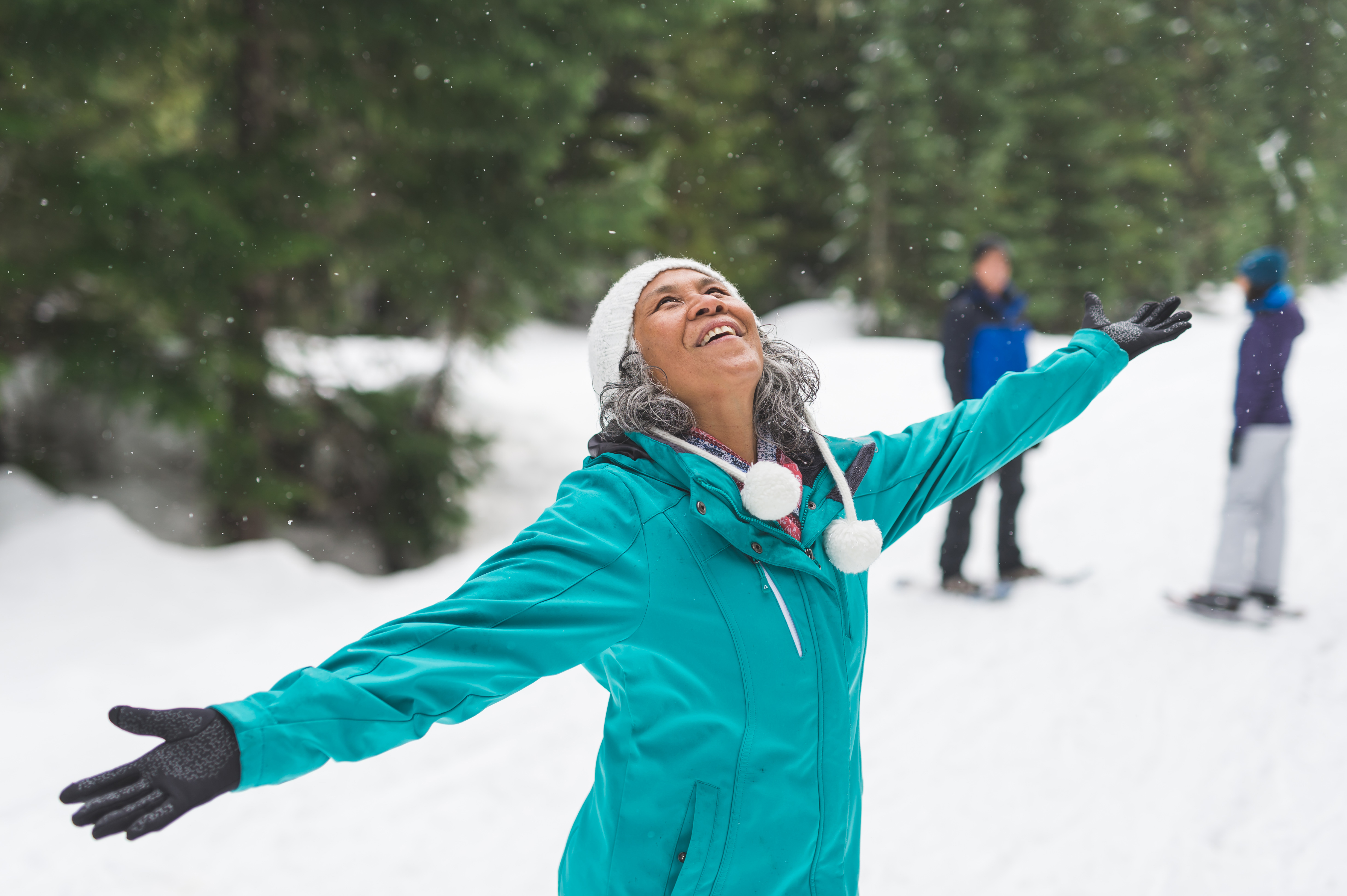 Older woman playing in the snow while a couple look on in the background